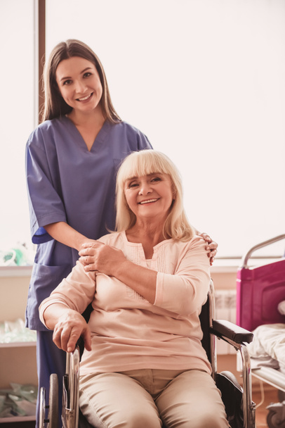 美しい老婦人がカメラを見て、近く魅力的な看護師は、病棟に車椅子に座りながら笑みを浮かべて、 - 写真・画像