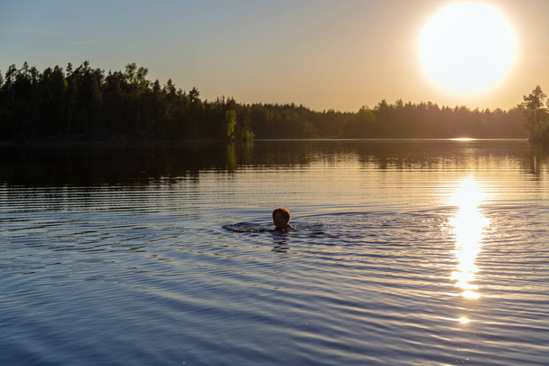 woman is swimming in a forest lake at sunset - 写真・画像