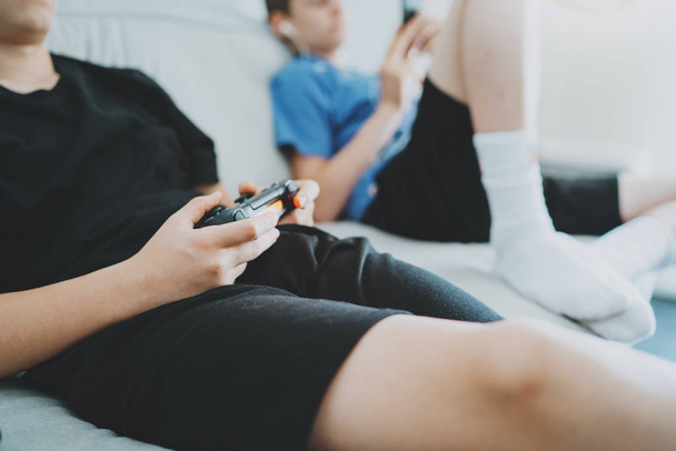 Brothers sitting on a sofa in living room and playing video games. Family relaxing time at home concept. - Fotó, kép