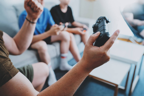Young best friends sitting on a sofa in living room and playing video games. Family relaxing time at home concept. Cropped. - 写真・画像