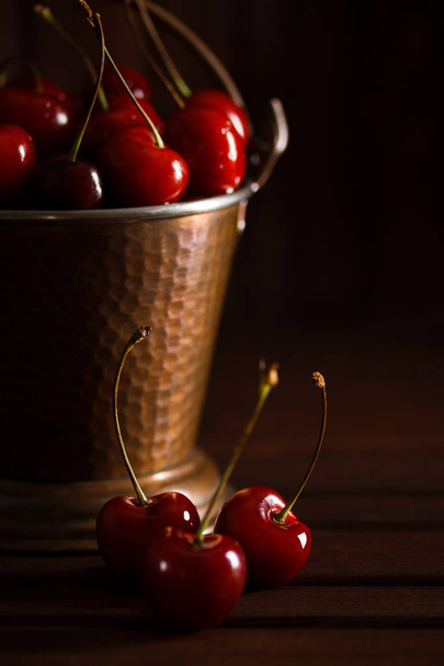 frische rote Kirschen im Kupfereimer auf dunklem Holzgrund. Sommer, - Foto, Bild