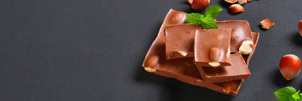 Шоколад з лісовими горіхами, м'ятою та зернами кави на темно-сірому столі
 - Фото, зображення