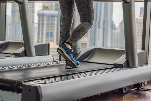 Beauty young woman exercising on treadmill in gym against the background of a big city. Sport, fitness, lifestyle, technology and people concept.  - Photo, image
