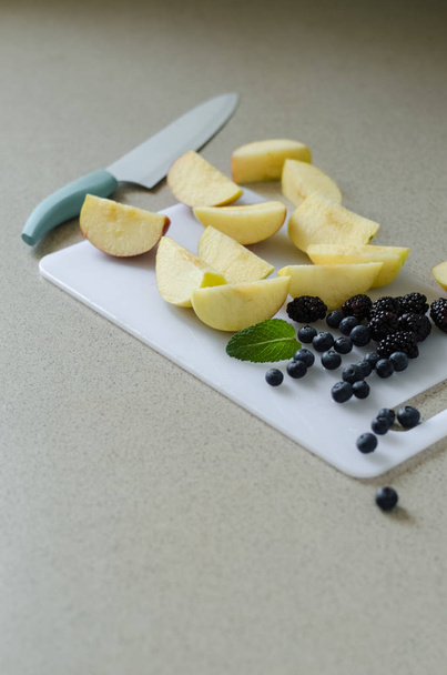 Sliced fresh apples, berries and mint leaves around, kitchen knife on side, fresh summer fruits from market - Foto, Imagem
