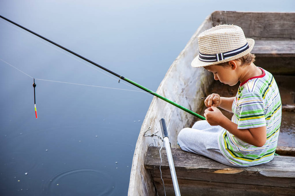 Молодий рибалка ловить рибу з човна на риболовлі, хлопчик змінює приманку на гачок
 - Фото, зображення