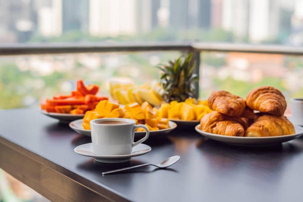 Breakfast table with coffee fruit and bread croisant on a balcony against the backdrop of the big city - Zdjęcie, obraz