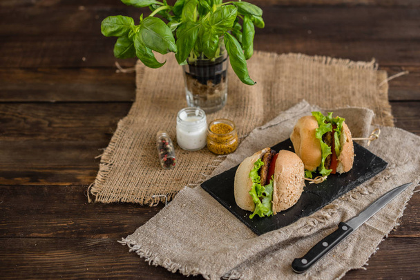 Smakelijke hamburger met vlees en groenten tegen een donkere achtergrond. Fast food. Het kan worden gebruikt als achtergrond - Foto, afbeelding