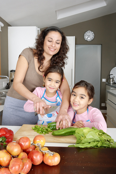 dzieciaki rodziny uczenia się posiekać warzywa w kuchni z mamą, uśmiechając się. - Zdjęcie, obraz