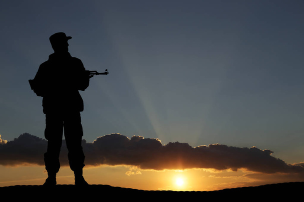 Silhouette eines Soldaten mit Gewehr im Sonnenuntergang - Foto, Bild