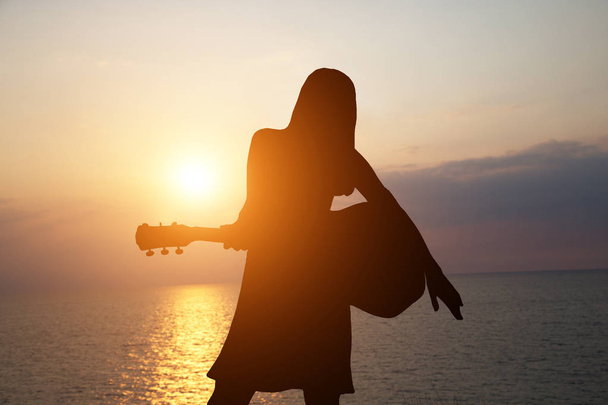 海を背景にギターを弾く少女のシルエットと美しい夕日 - 写真・画像