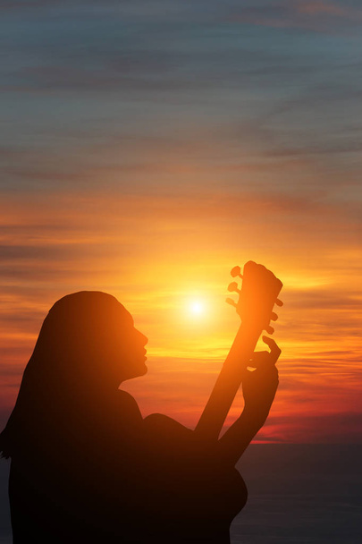Gitar çalan kızın silueti denizin arka planında ve güzel bir günbatımı - Fotoğraf, Görsel