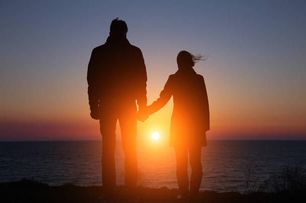 sziluett srác és lány egy gyönyörű naplementében fogja egymás kezét - Fotó, kép