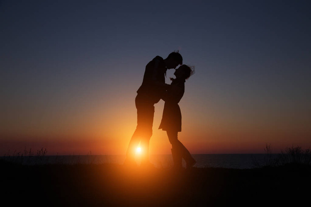 sylwetka facet i dziewczyna na piękny zachód słońca trzymając się za ręce - Zdjęcie, obraz