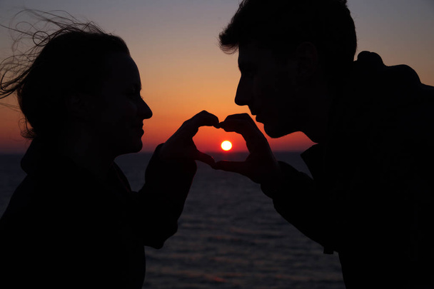 sziluett srác és lány egy gyönyörű naplementében fogja egymás kezét - Fotó, kép