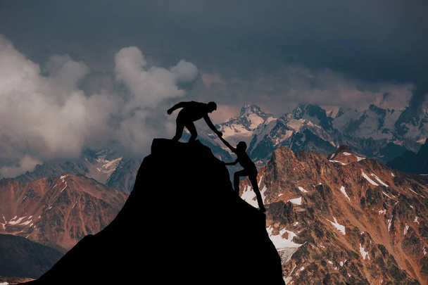 Senderistas masculinos y femeninos subiendo por el acantilado de la montaña y uno de ellos dando una mano amiga. Personas ayudando y, concepto de trabajo en equipo
. - Foto, imagen