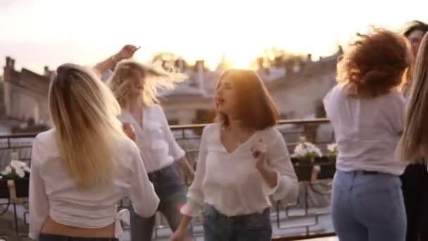 Six women are hanging out together on the terrace. All in the same style clothes. Dancing and jumping. Casual clothes. Cityscape background. Hen party concept. Dusk. Slow motion - Footage, Video