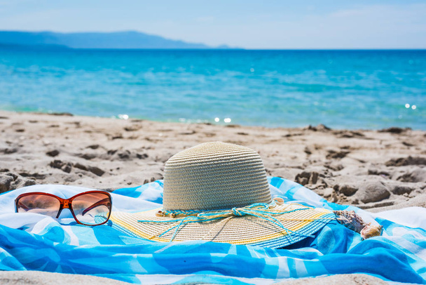 Ψάθινο καπέλο και γυαλιά ηλίου στην άμμο δίπλα στη θάλασσα - Φωτογραφία, εικόνα