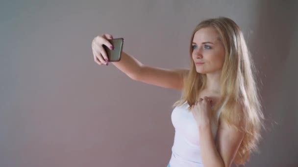 Beautiful girl with light makeup takes a selfie on a gray background. - Video, Çekim