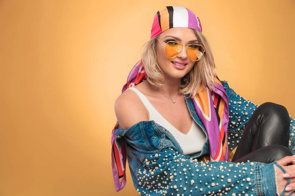 portrait of beautiful woman with yellow sunglasses and colorful headscarf sitting on yellow background with legs at her chest - Foto, afbeelding