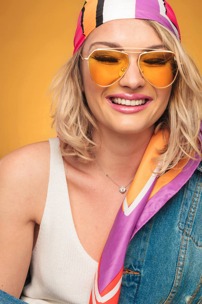 close up of rock woman with yellow sunglasses and denim shirt laughing with eyes closed on yellow background - Foto, afbeelding