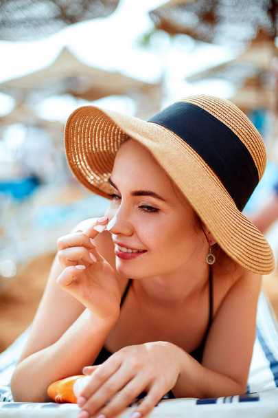 Suntan   woman in hat applying sunscreen solar. Beautiful happy woman smear  lotion  with sun cream   to her nose. Skincare.  - Photo, Image