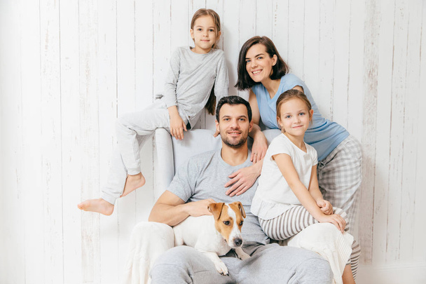 Friendly family of four memebers: cheerful European brunette female, her husband, two daughters and favourite pet, have good relationships, support each other. Affectionate parents with children - Photo, Image