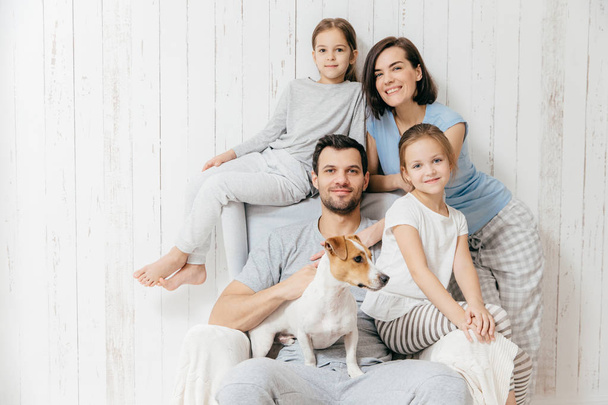 Portret rodziny. Szczęśliwych rodziców z ich dwie córki i pies stanowią razem białym tle, spędzić wolny czas w domu, będąc w dobry nastrój. Matka, ojciec i małe siostry stwarzają kryty - Zdjęcie, obraz