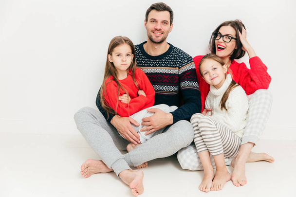 4 人のメンバーの幸せな家族の肖像画: 魅力的なブルネットの女性、彼女の夫および 2 人の小さい娘が白い背景で隔離を床に座る。親概念。屋内の素敵な家族. - 写真・画像