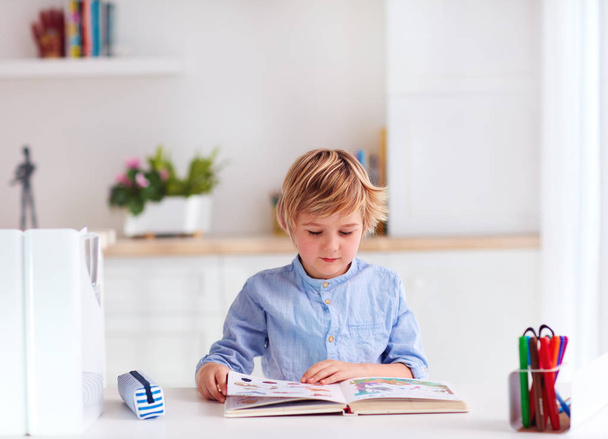 young kid, boy reading a book while sitting at the desk at home - Foto, imagen