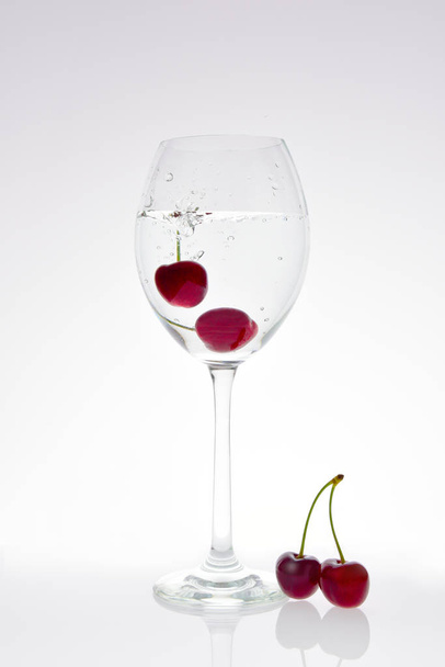 Cherries fall into a glass with sparkling water - Zdjęcie, obraz