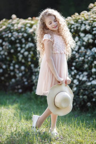 Portrait beautiful happy girl enjoying smell in a flowering spring blooming garden. Bright and fashionable smiling girl near blossom beautiful bush tree with white flowers in spring garden. Landscape. Spring portrait of a smiling girl in a hat - Photo, image