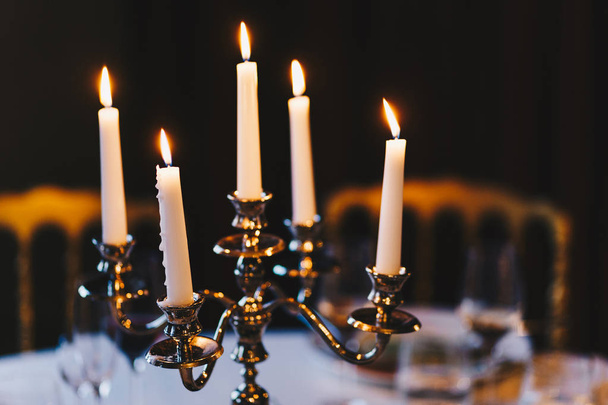Burning candles on bronze candlestick against dark background at home. Vintage style. Calm romantic atmosphere. Horizontal image for design. - Fotografie, Obrázek
