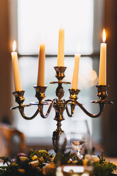 Photo of antique candlestick stands on festive table with wonderful decoration. Cozy atmosphere. Burning candles used for decor. Romantic dinner - Photo, Image