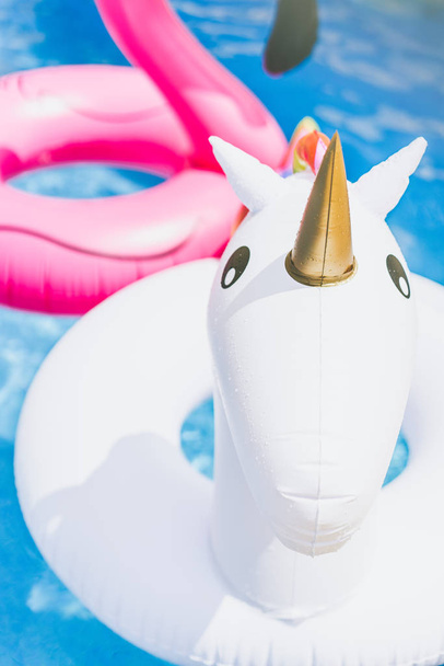 Надувной красочный белый единорог и розовый фламинго в бассейне. Отдых в бассейне с пластиковыми игрушками. Отдых и развлечения по вертикали
. - Фото, изображение