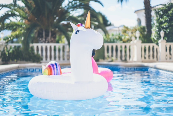 Inflatable colorful white unicorn and pink flamingo at the swim pool. Vacation week in the swimming pool with plastic toys. Relaxation and fun concept. - Фото, изображение