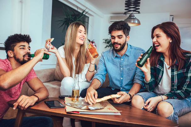 Grupo de jovens amigos comendo pizza, bebendo cerveja e assistindo TV em casa
. - Foto, Imagem
