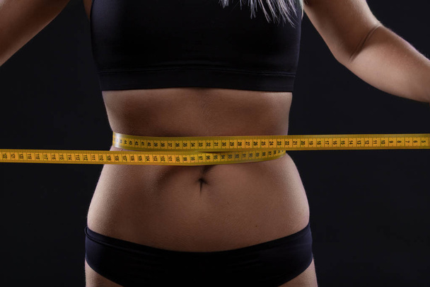 Atletische slanke vrouw haar taille meten door maatregel band na een dieet op zwarte achtergrond. - Foto, afbeelding