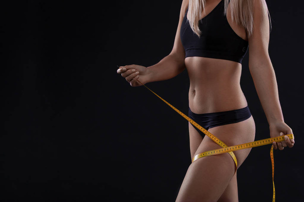 Volume legs with measuring tape. Woman after diet slimming weight loss on black background. Copy space - Photo, Image