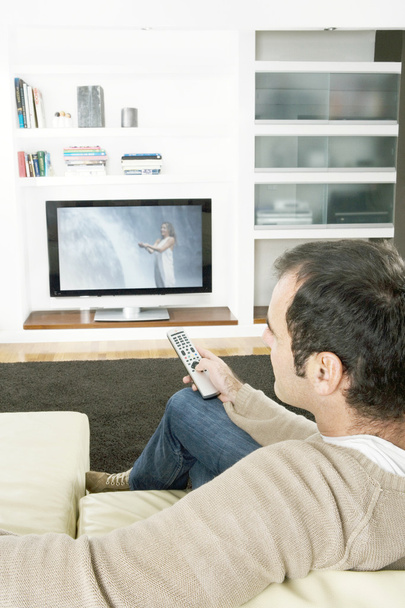 Homme professionnel utilisant une télécommande de télévision pour changer de chaîne à la télévision à la maison
. - Photo, image