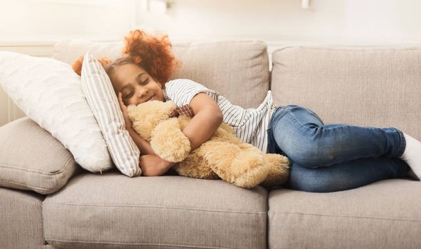 Pequeña chica afroamericana feliz durmiendo en el sofá en casa
 - Foto, imagen