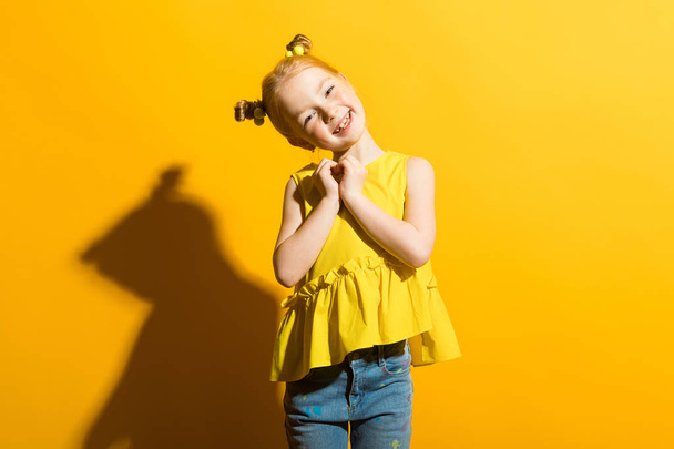 Girl with red hair on a yellow background. The girl clasped her heart. - Foto, immagini