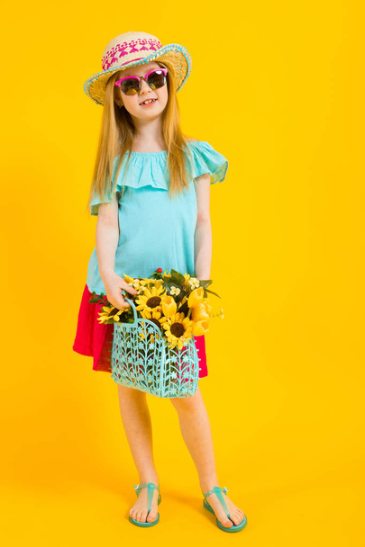 Girl with red hair on a yellow background. A charming girl in bright summer clothes is holding a basket of sunflowers in her hands. - Foto, Bild
