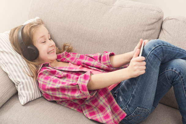 Szczęśliwa dziewczynka przy użyciu smartfona na kanapie w domu - Zdjęcie, obraz