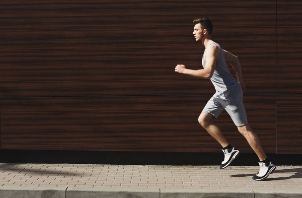 Молодой мускулистый человек бегает по городу, темно-деревянный фон стены, пространство для копирования, вид сбоку
 - Фото, изображение