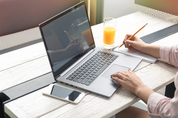 Close up retrato de uma jovem mulher trabalhando em laptop e escrita, suco de laranja na mesa
. - Foto, Imagem