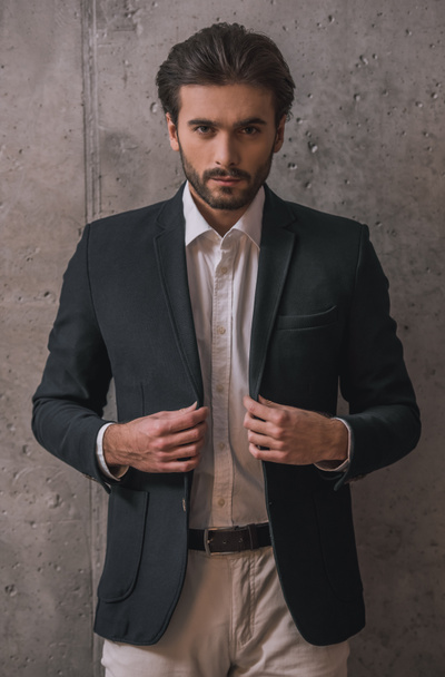 schöner selbstbewusster Geschäftsmann mit Borsten, im Anzug, blickt in die Kamera, auf grauem Hintergrund - Foto, Bild