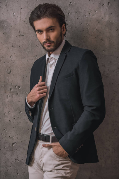 Handsome confident businessman with bristle, in suit, is looking at camera, on gray background - Foto, Imagem