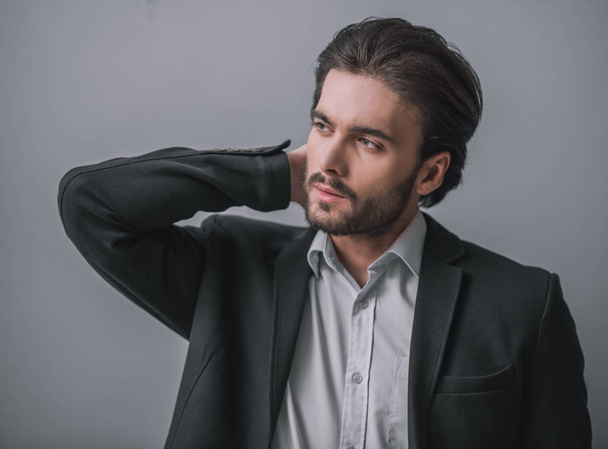 Handsome bearded businessman in suit is looking away, on gray background - Photo, Image