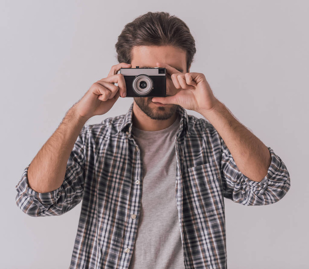 Knappe bebaarde man in casual kleding is met behulp van een fotocamera, op lichte achtergrond - Foto, afbeelding