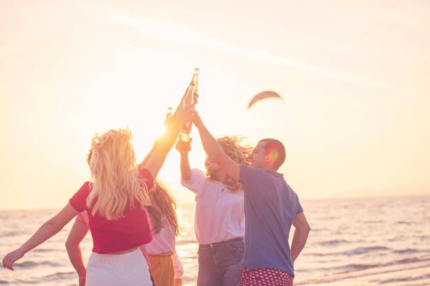 Gruppe fröhlicher junger Leute mit Getränken am Strand bei schönem Sommersonnenuntergang - Foto, Bild
